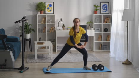 aerobics-and-gymnastics-training-at-home-teen-girl-is-crouching-on-legs-on-sides-fitness-in-living-room-doing-exercises-for-health-of-body